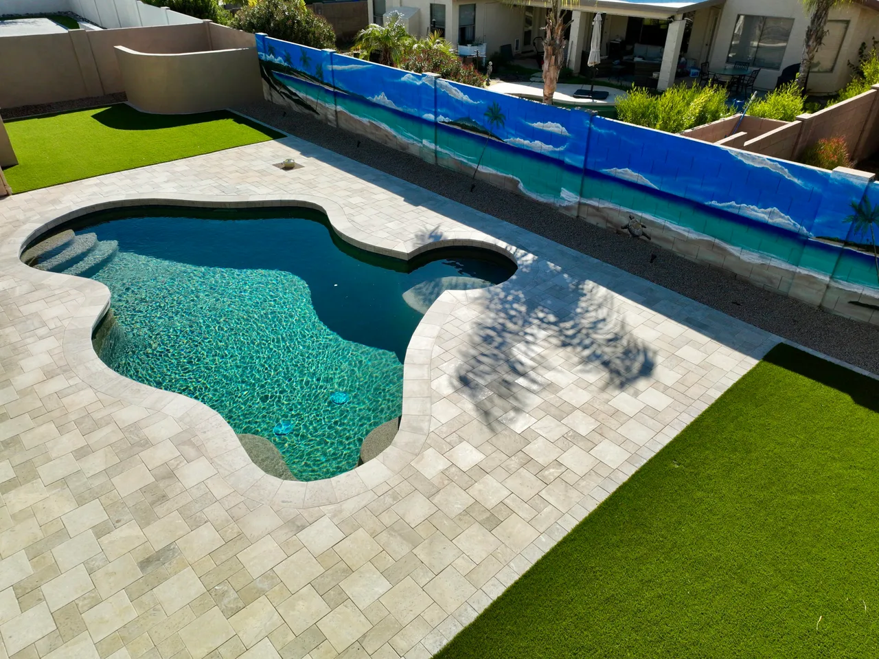 Freeform pool with pale paver decking and artificial turf