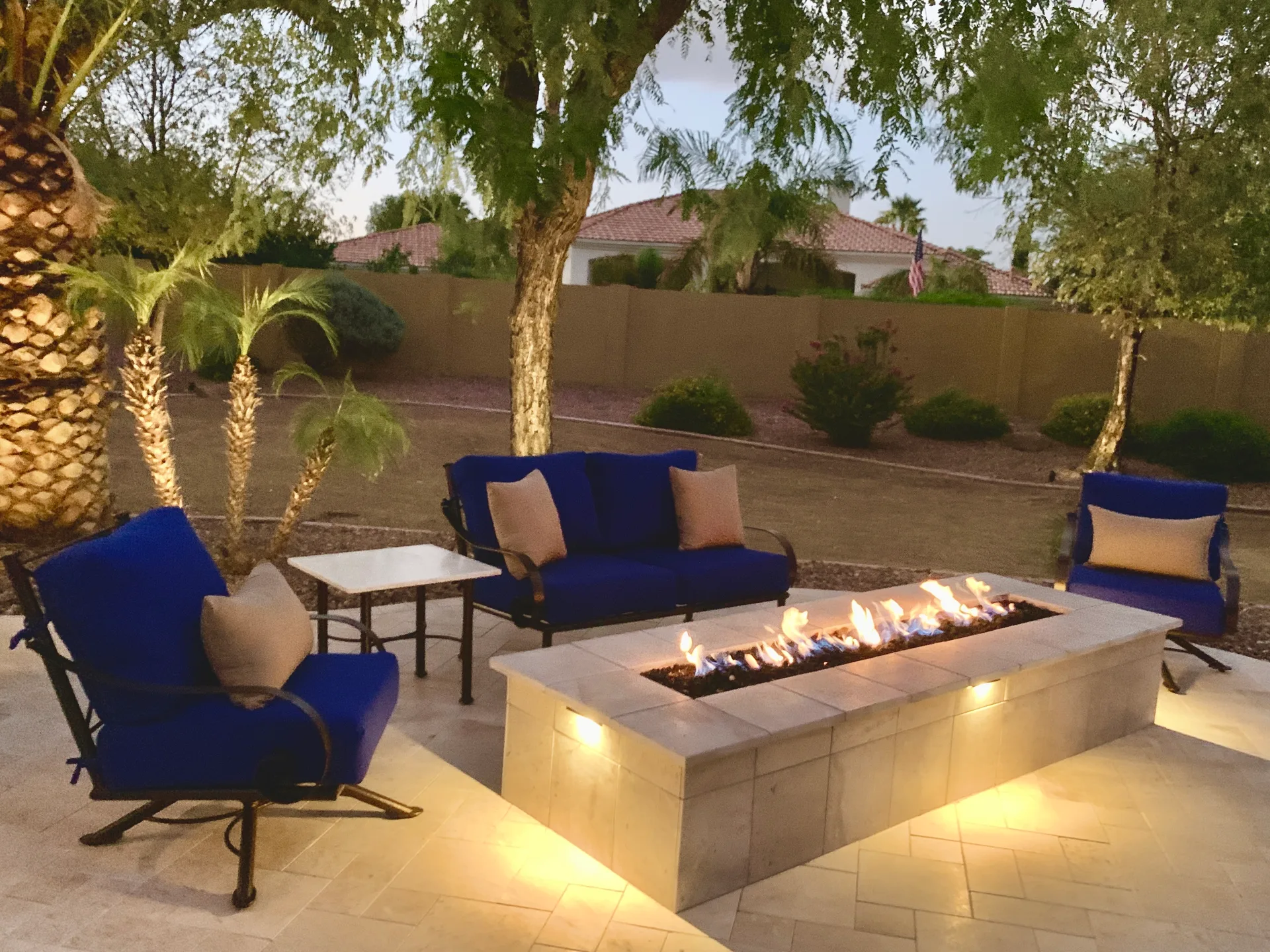 Linear fire pit at dusk with blue seating on travertine pavers