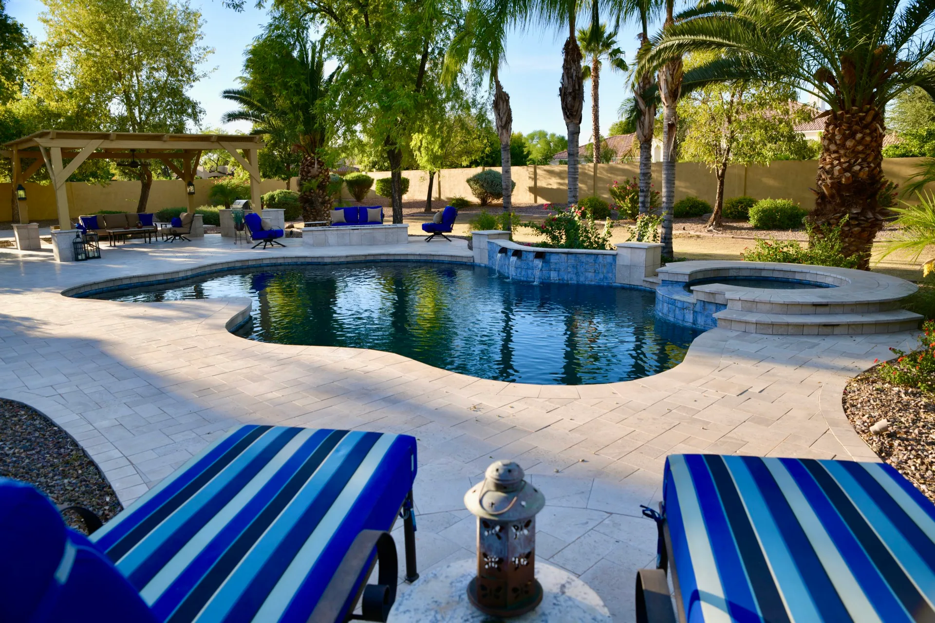 Pool with a raised spa, water feature wall and wood ramada among palms